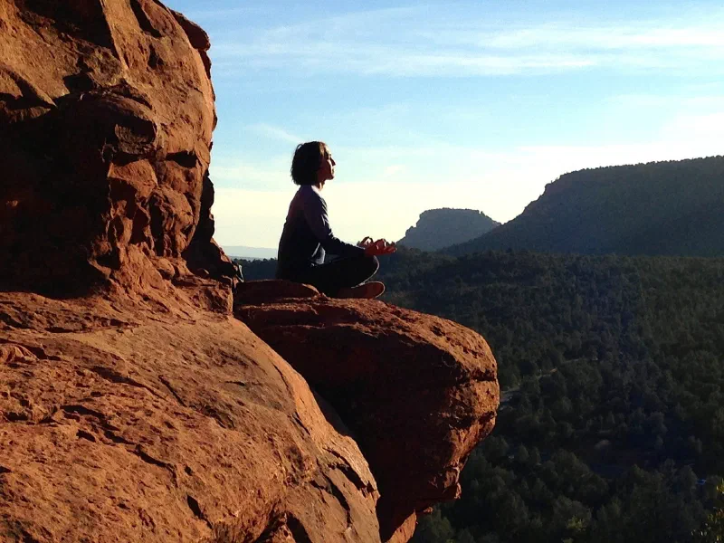 Person meditating on a red rock ledge above a forested valley