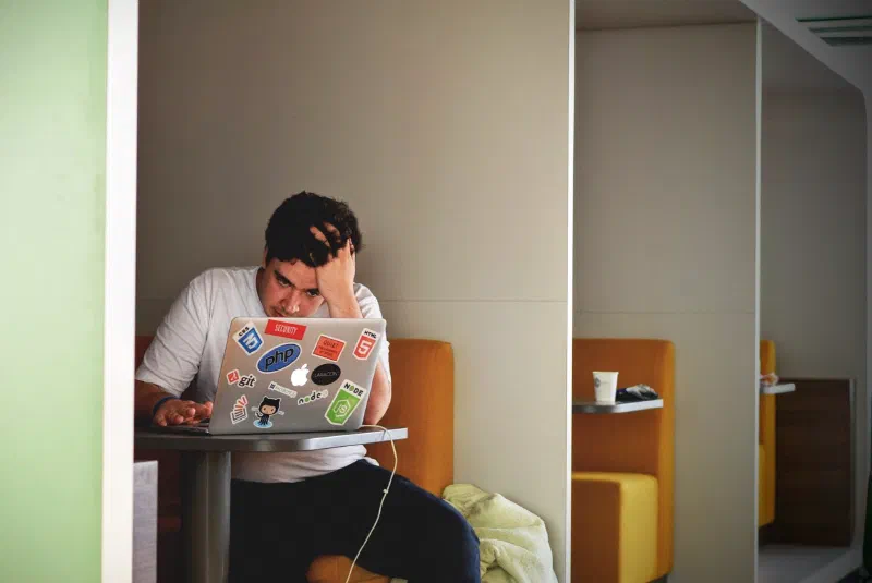 Developer holding his head while looking at a laptop covered in stickers