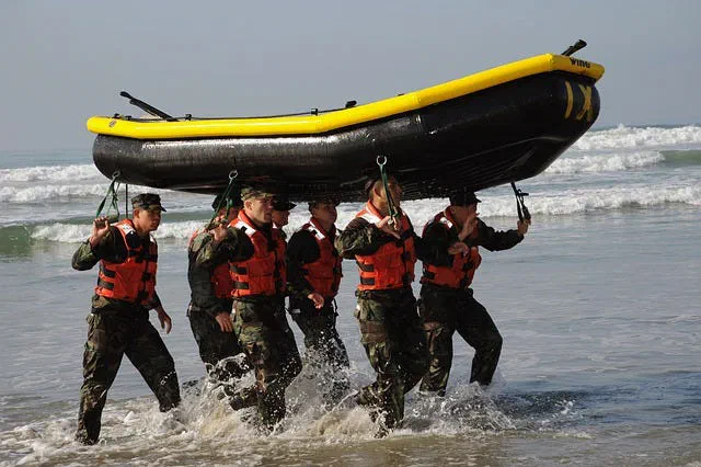 Group of people in life vests carrying an inflatable boat on their heads through surf