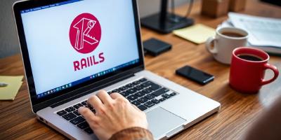 Developer typing on laptop with Ruby on Rails logo.